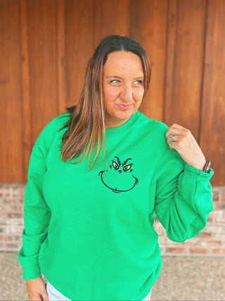 Green Christmas crewneck with embroidered Grinch face, modeled by an A Gathering Place team member